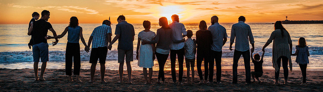 Eine Gruppe befindet sich am Strand und schaut sich den Sonnenuntergang an. 