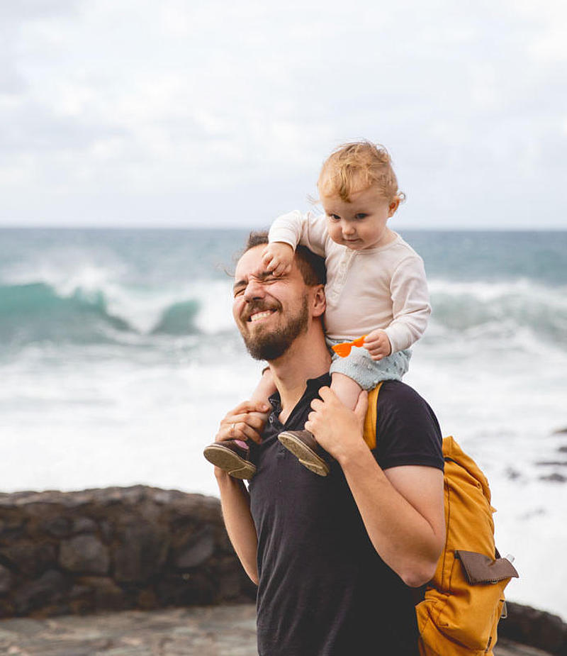 Junges Kind sitzt auf den Schultern seines Vaters am Strand.