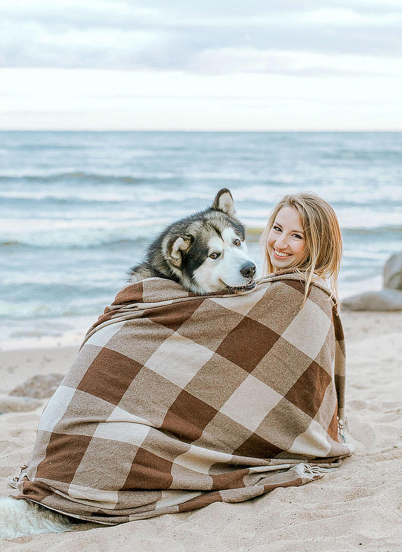 A woman sits on the beach with her dog